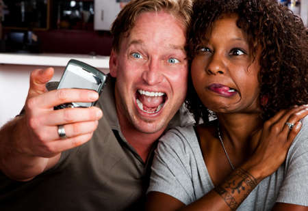Caucasian man and African American woman taking picture in coffee house with cell phoneの写真素材