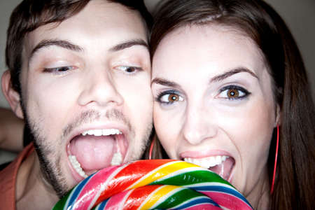 Cute Couple Biting into Big Colorful Lollipopの写真素材