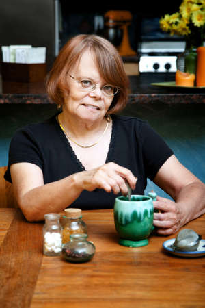 Senior woman at table stirrung cup of herbal teaの写真素材