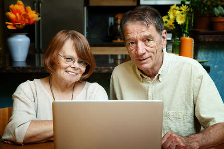 Senior couple using silver laptop computer at homeの写真素材