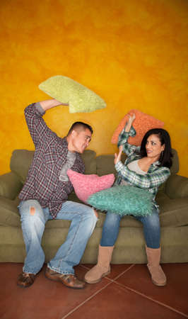 Hispanic couple on couch play fighting with pillowsの写真素材