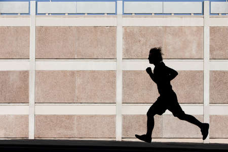 Man in the shadows of building runs for exercise.の写真素材