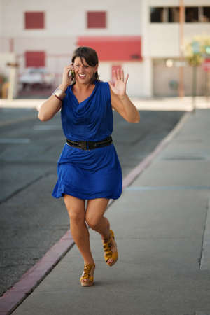 Woman runs down the street while having a cell phone conversation.の写真素材