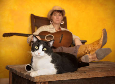 Pretty western woman in antique rocking chair with guitar and catの写真素材