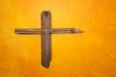 Rugged wooden cross hanging on yellow wallの写真素材