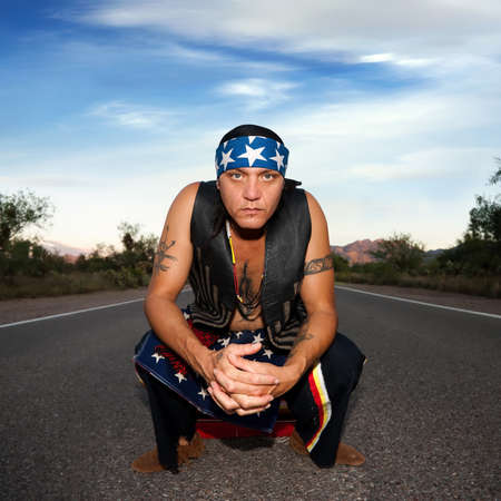 Indigenous man squatting in the middle of a road