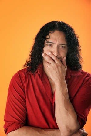 A handsome, muscular Native American man with curly hair and a red shirt looking sad or depressed