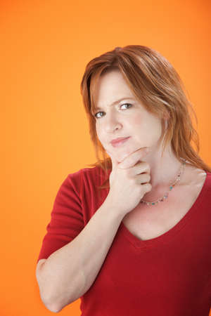 A cute woman holding her chin on an orange background