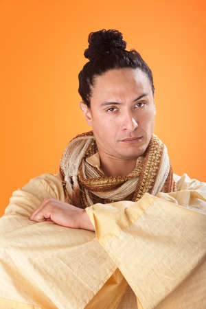 A serious looking japanese samurai on orange background with folded handsの写真素材