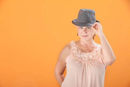 Middle-aged Caucasian woman on orange background tips her hat