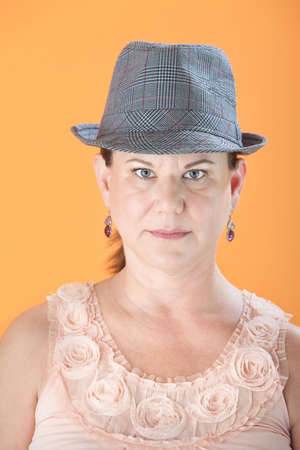 Serious Caucasian woman with hat on orange background