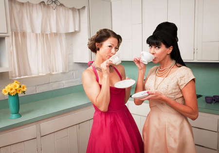 Two retro-styled women drinking coffee in kitchenの写真素材