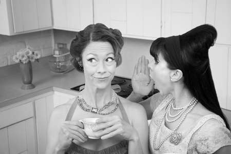 Retro styled woman whispers secret into friend's earの写真素材