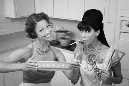 Happy housewife shows her smoking friend a dish in the kitchenの写真素材