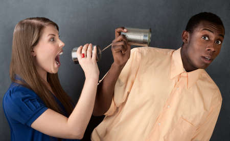 Woman shouts at a man through stringed cans on gray backgroundの写真素材