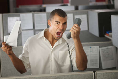 Frustrated office worker yelling on phone in his cubicle の写真素材