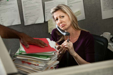 Unhappy woman employee given a stack of files の写真素材