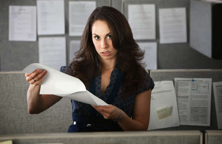 Frustrated woman office worker holding documents stands in cubicle