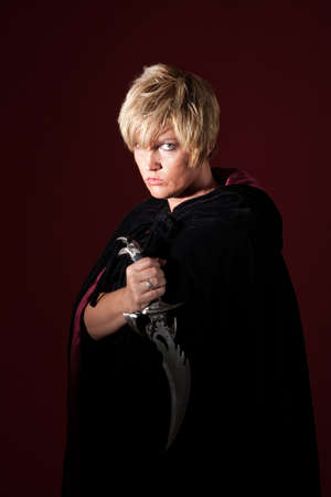 Evil woman holds sharp knife over maroon background