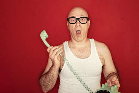 Shocked bald Caucasian man holds telephone over maroon backgroundの写真素材