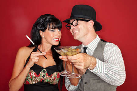 Happy Caucasian couple enjoy martini and cigarette over maroon background