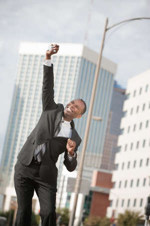Excited Black businessman with phone in hand leaps in their airの写真素材