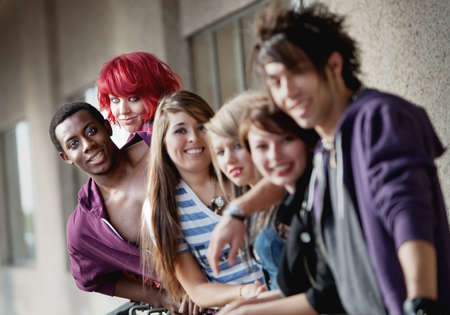 Punk rock looking teens smile at the camera as the camera focuses on the back two individuals.