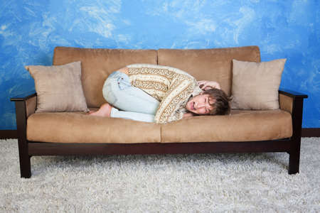 Scared Caucasian teen in curled up position on sofa