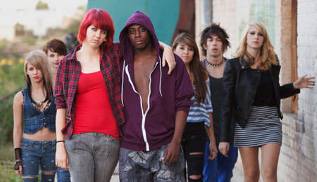 A pair of young punk teens pose together as their friends stay in the background. A pair of young punk teens pose together as their friends stay in the background.