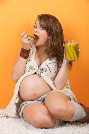 Happy pregnant woman on the floor eating picklesの写真素材