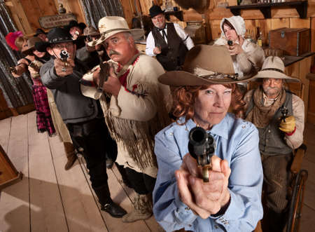 Armed senior woman and crowd points guns in old saloon