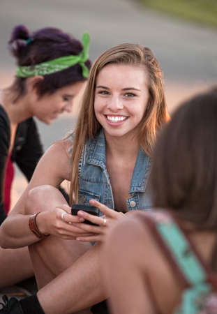 Cute European teenage girl sitting on ground with phoneの写真素材
