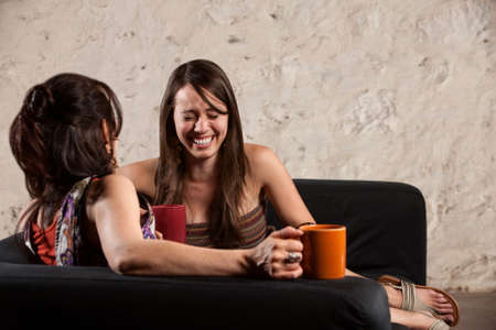 Emotional young lady sitting with friend on sofa indoorsの写真素材
