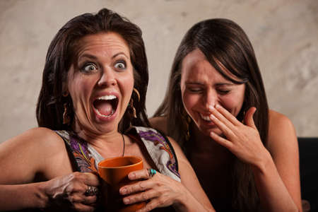 Screaming woman holding coffee mug next to laughing friend 