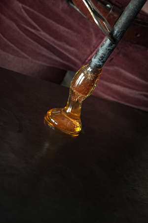 Hot molten yellow glass oozing on table from rod