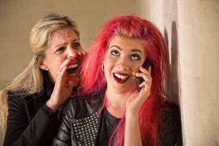 Mature woman yelling to ear of teenager on phoneの写真素材