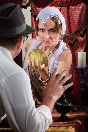 Fortune teller holding crystal ball in front of scared manの写真素材