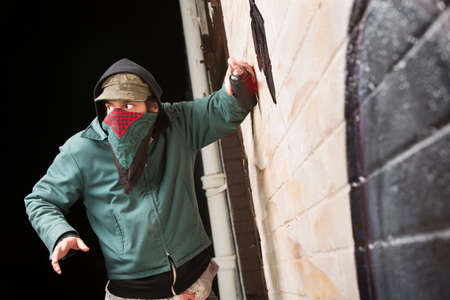 Scared disguised criminal defacing a wall outdoors