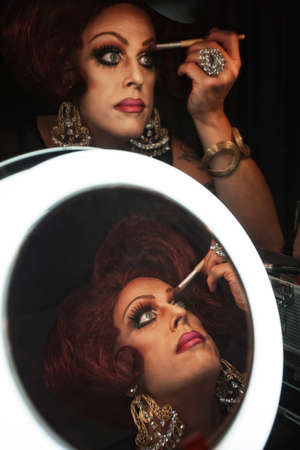 Cross dressing man putting on makeup at a mirrorの写真素材