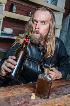 Drunk Western Man Aims Gun Towards Bottle as he Sits at Tableの写真素材