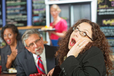Business woman yawning as man talks to her during lunchの写真素材