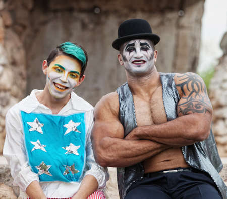 Laughing clown with stars and muscular man in hat