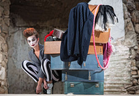 Grinning female clown squatting near stack of suitcasesの写真素材