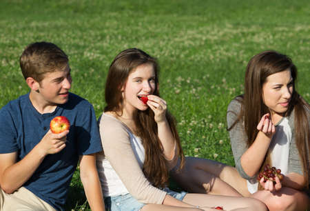 Trio of happy Caucasian teenagers eating fruit outdoorsのeditorial素材