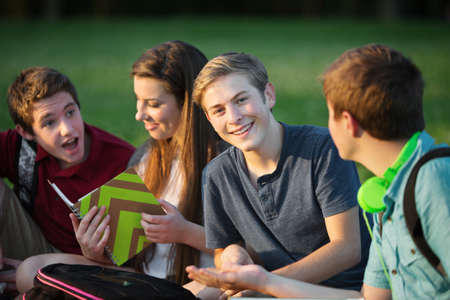 Happy male teen sitting with students outdoors
