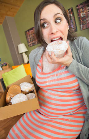 Happy pregnant woman making a mess eating donutsの写真素材