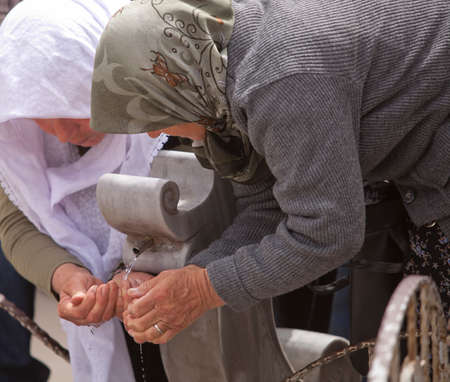 Two women catching water from public fountain in Turkeyの写真素材