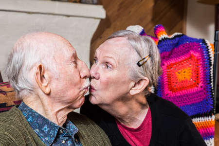 Happy elderly couple sitting in livingroom kissingの写真素材