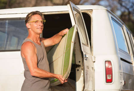 Single handsome man removing surfboard from of his vanの写真素材