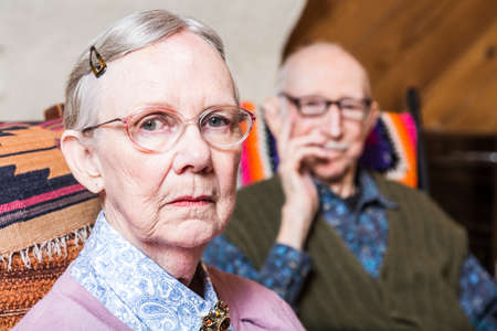 Elderly couple looking seriouds seated in livingroomの写真素材